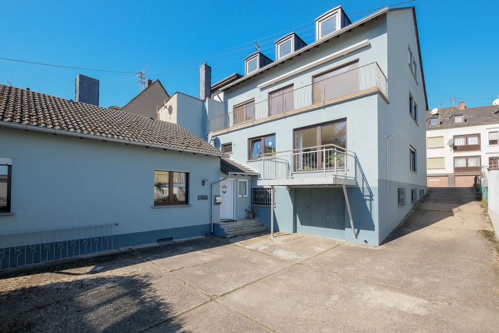 Multi-story residential building with light blue facade and small balcony, surrounded by other buildings under a clear blue sky.
