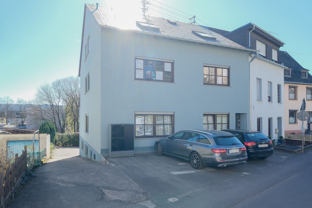 A light gray residential building with parked cars in the driveway parking area on a sunny day.