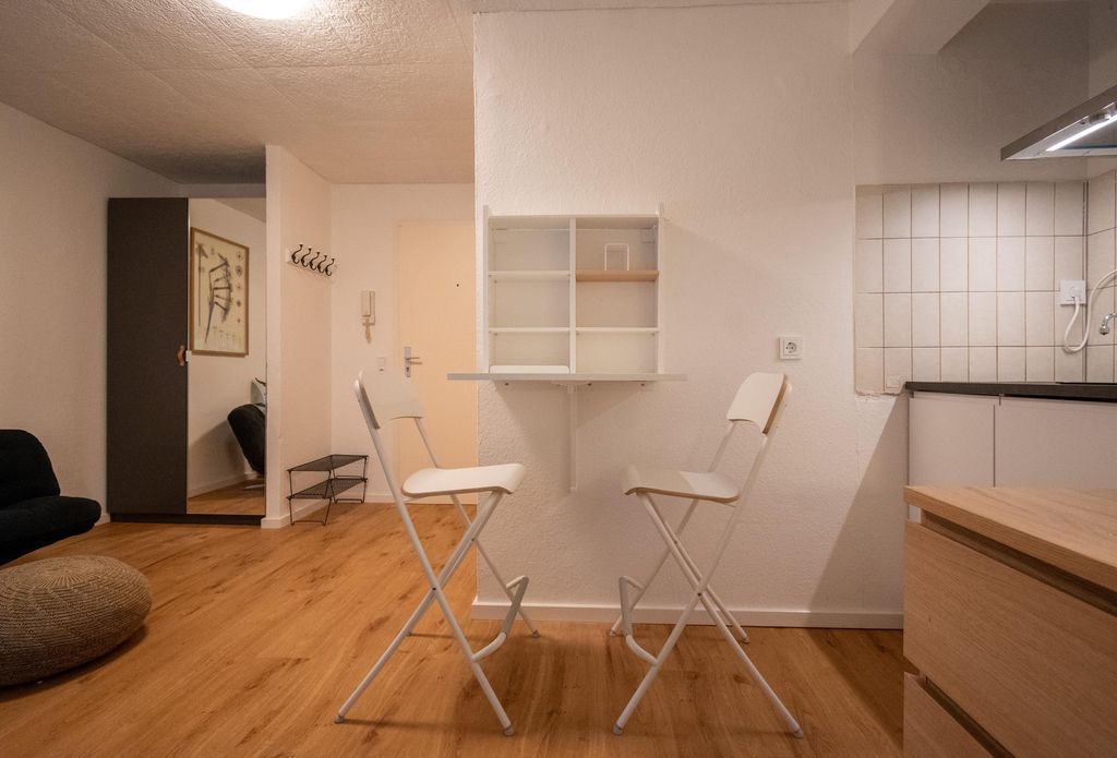 Two white folding chairs facing a small wall-mounted cabinet in a modern room with wooden flooring.