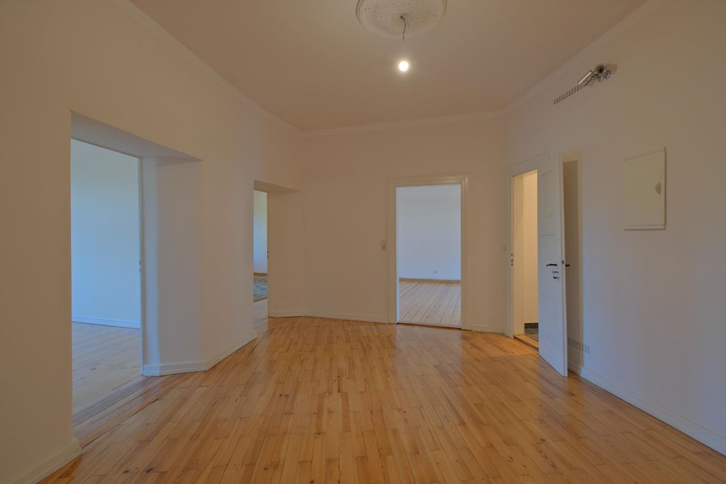 Empty room with wooden floor and white walls, four open doorways leading to adjacent rooms, a single light bulb hanging from the ceiling.