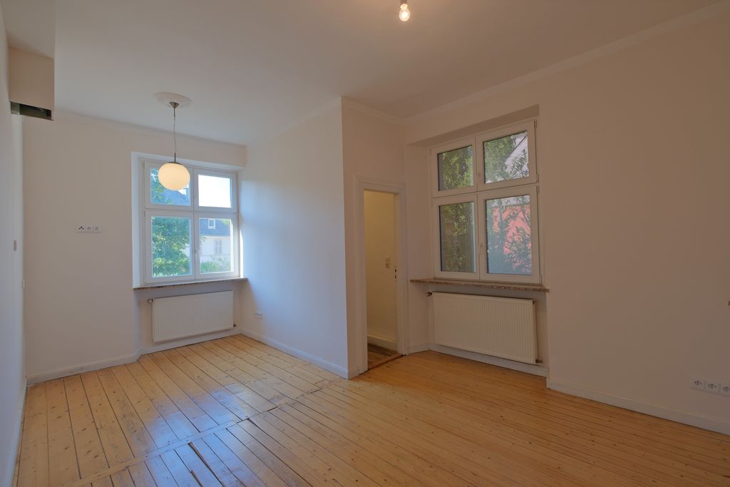 Empty room with two windows, wooden floor, and white walls, featuring a round ceiling light and an open passage to an adjacent room.