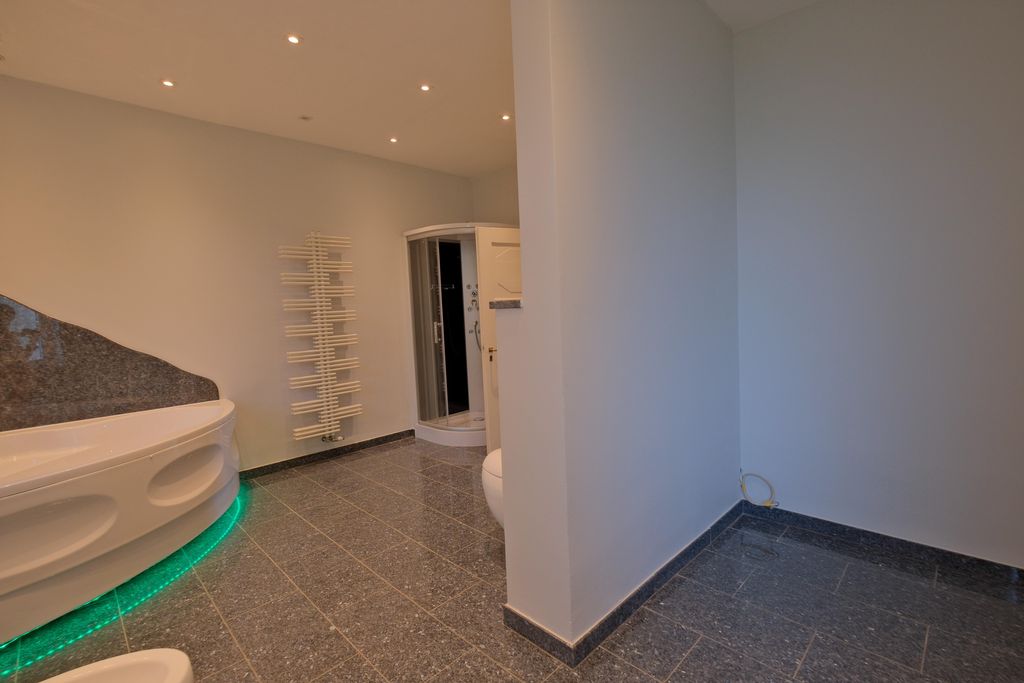 Modern bathroom featuring a corner bathtub with green LED underlighting, glass door shower, and a white radiator on the wall.