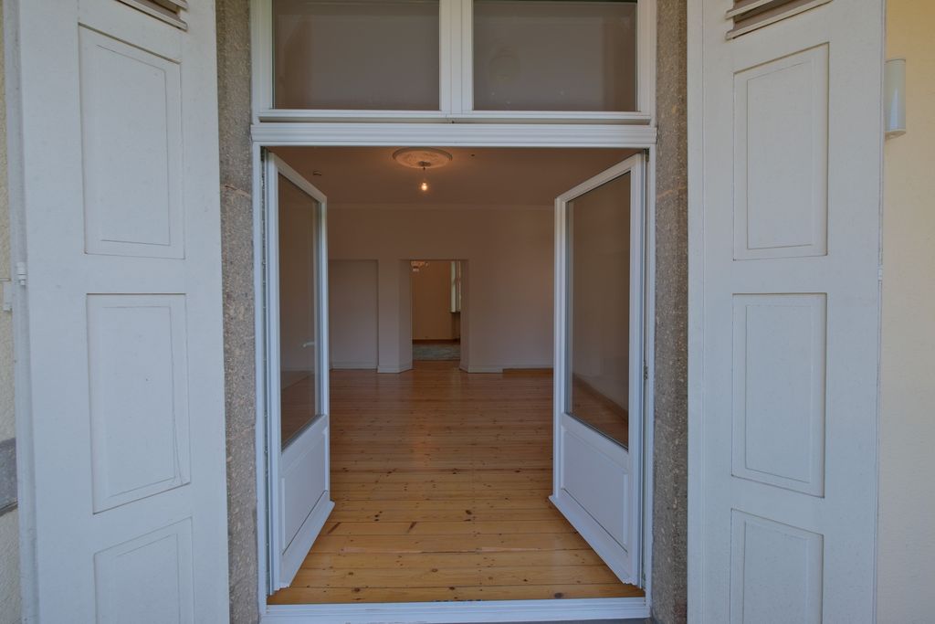 Open white double doors lead into a room with wooden flooring and white walls.