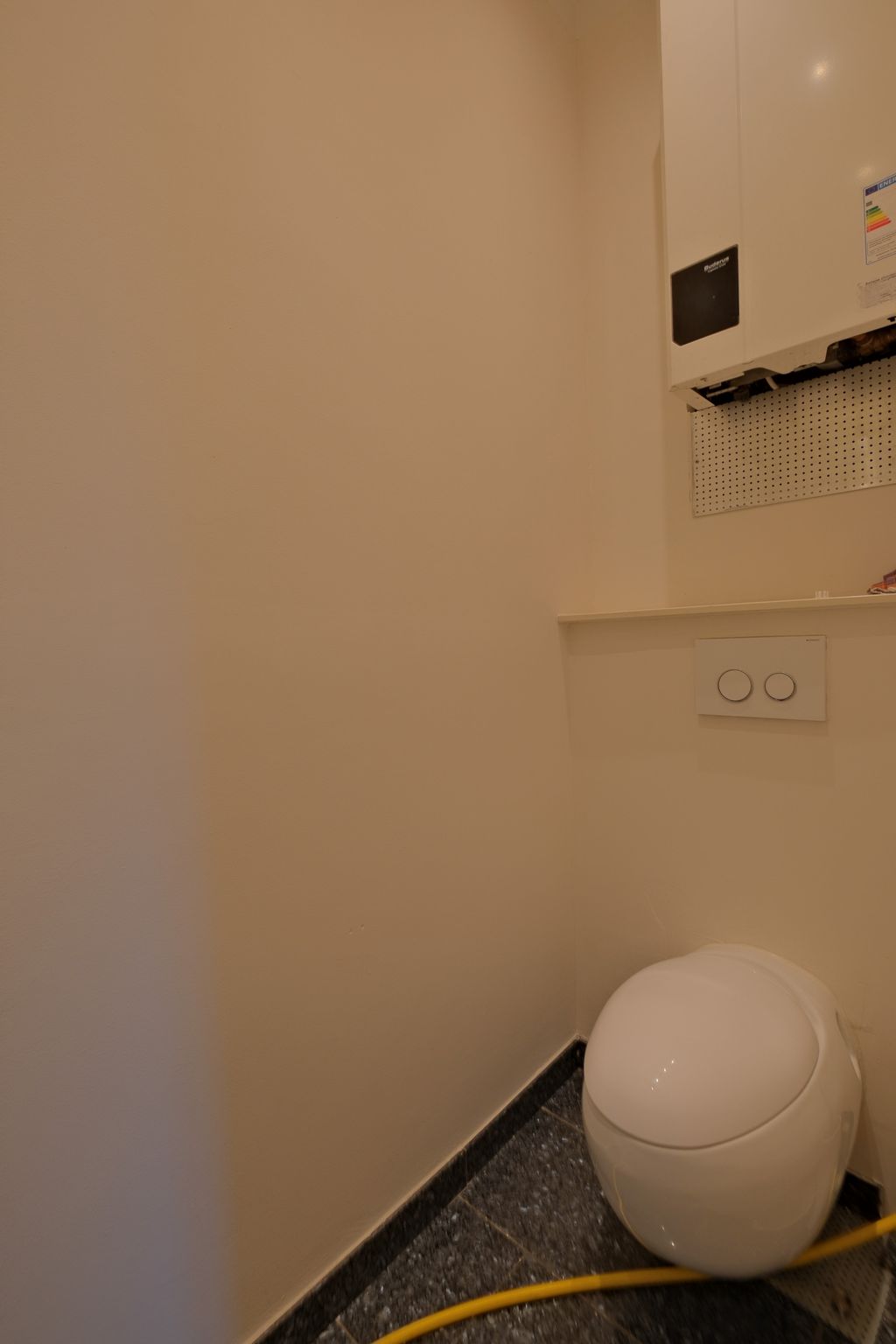 Modern toilet with a round, white design in a small bathroom with beige walls and black flooring.