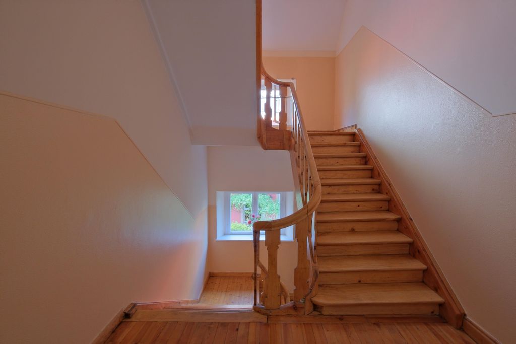 Interior staircase with wooden floor and wooden railing, white walls, and a window with an outdoor view.
