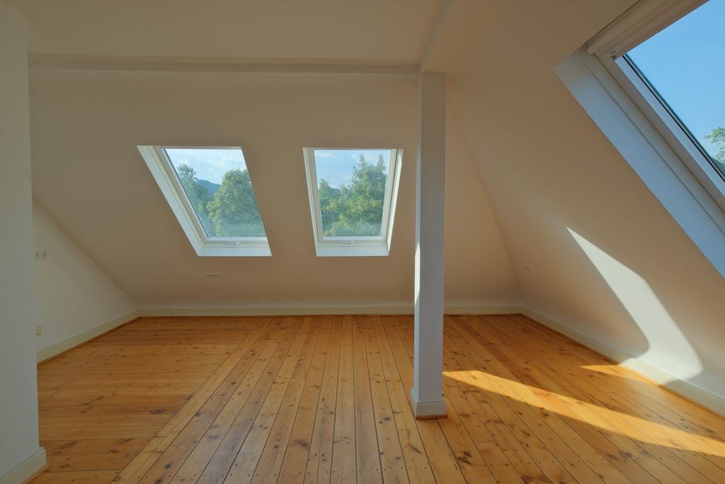 Empty attic room with large skylights, wooden flooring, and white walls illuminated by natural daylight.