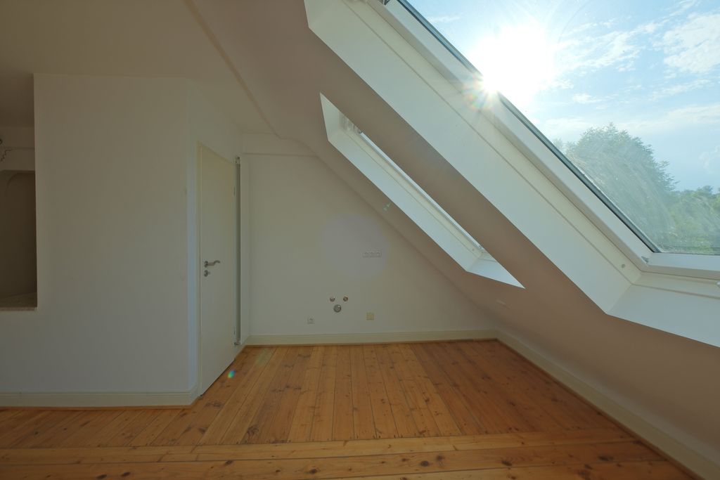Brightly lit empty room with slanted skylight window and wooden floor.