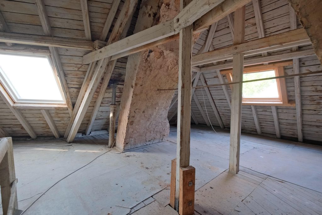 Empty attic with visible wooden beams, wooden paneling, and two large skylights letting in daylight.