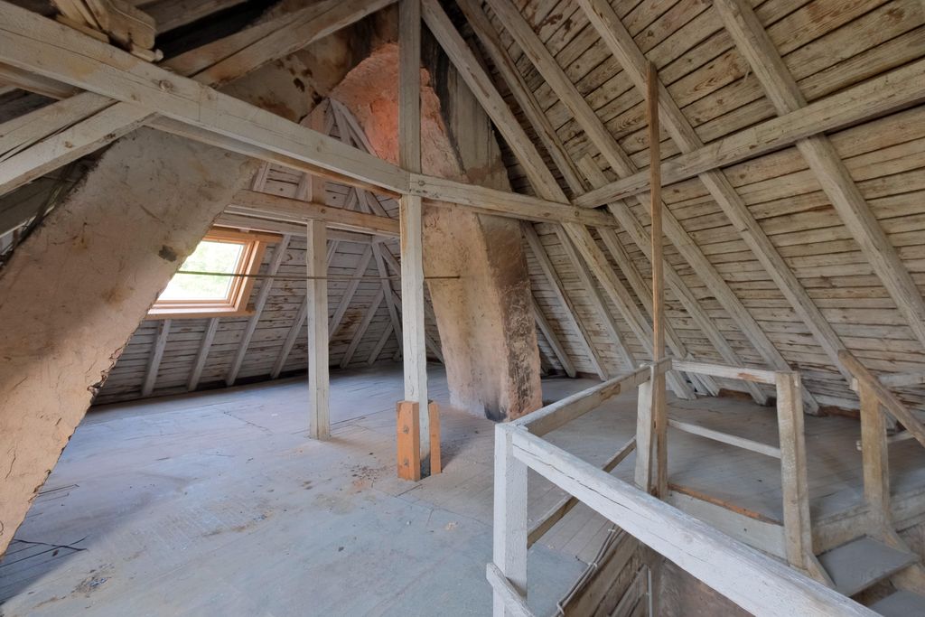 Attic with exposed wooden beams, a skylight, and a large plastered chimney inside the space.
