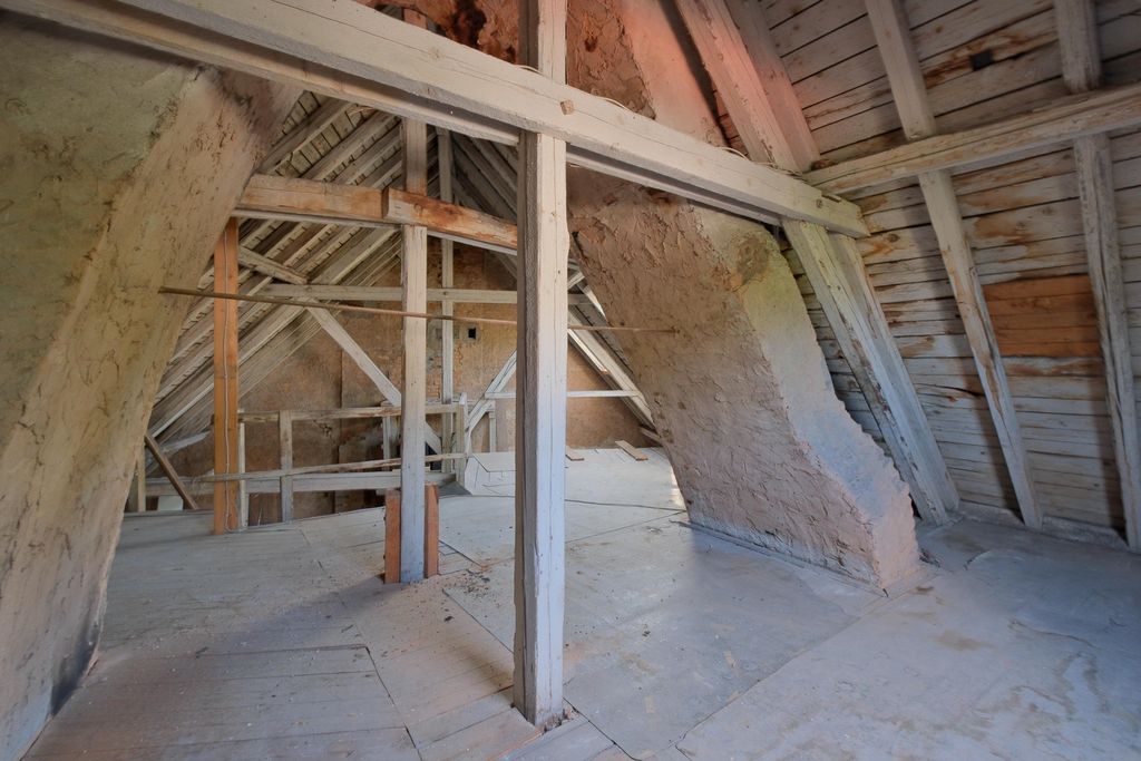 Old empty attic with visible wooden beams and slanted walls made of wood and plaster.