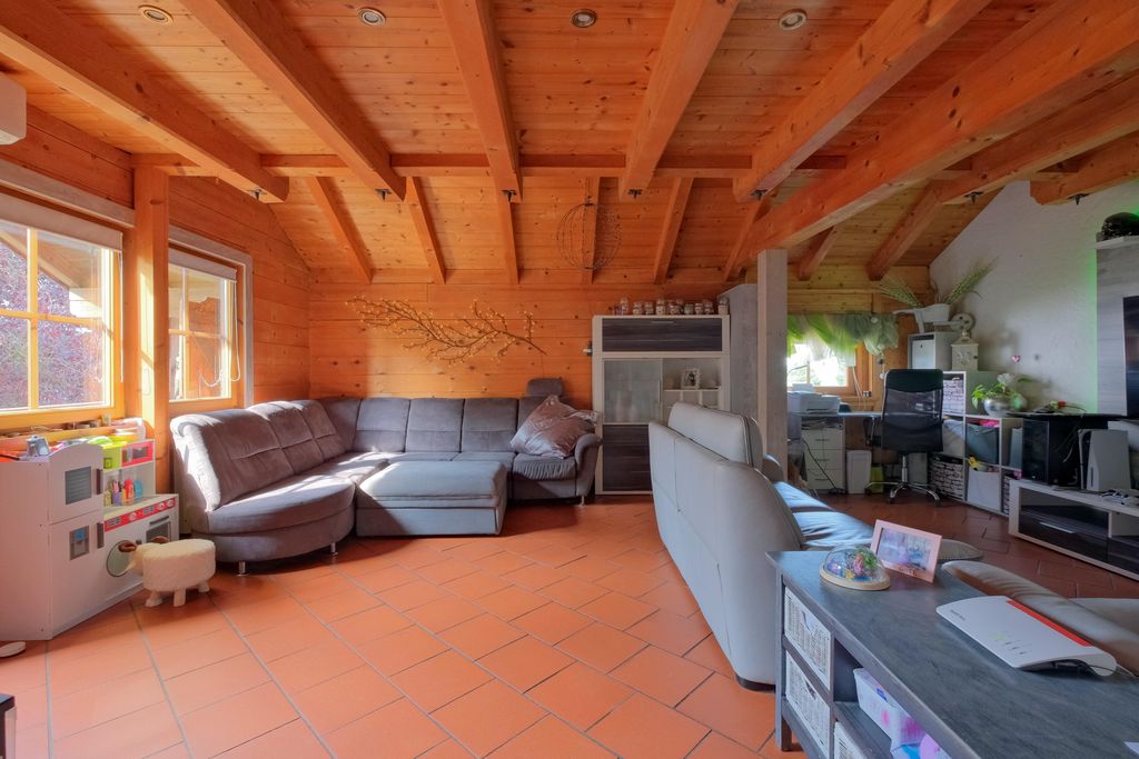 Spacious living room with wooden walls and exposed ceiling beams, gray sectional sofa, and a branch decoration on the wall.