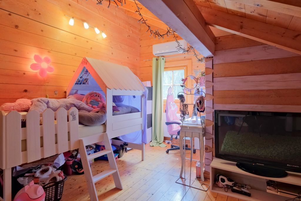 Children's room featuring a wooden loft bed shaped like a house, warmly lit with a flower wall lamp, a desk with a chair by the window, and a large TV in the room.
