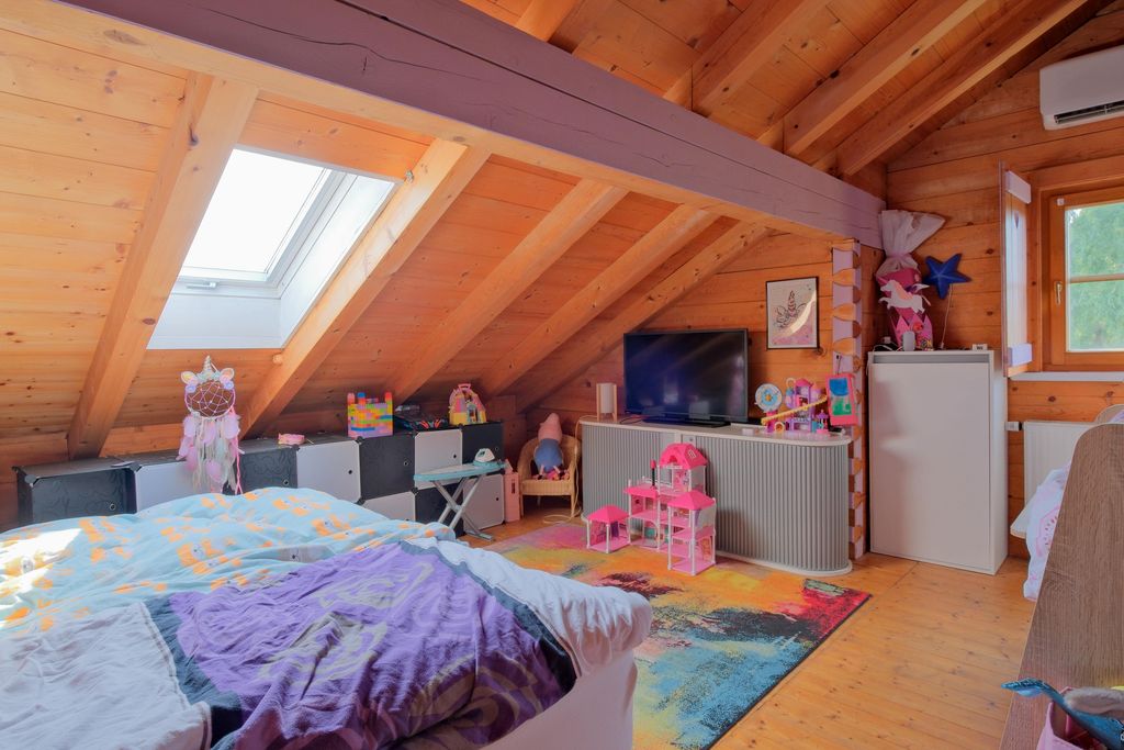 Children's room in an attic with wooden paneling, skylight, colorful rug, and various toys and furniture.