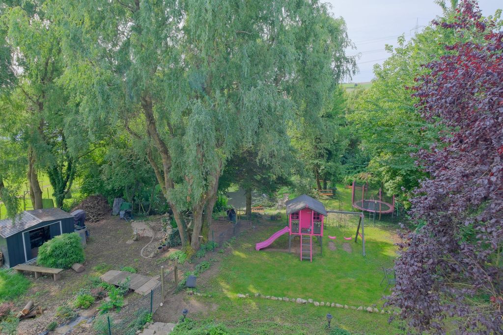 A playground with a pink climbing structure featuring a slide and swing next to a trampoline, surrounded by trees and greenery in a garden.
