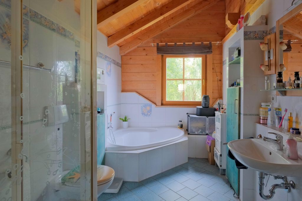 Bright bathroom with wooden ceiling, corner bathtub beneath a window, sink, and shower.