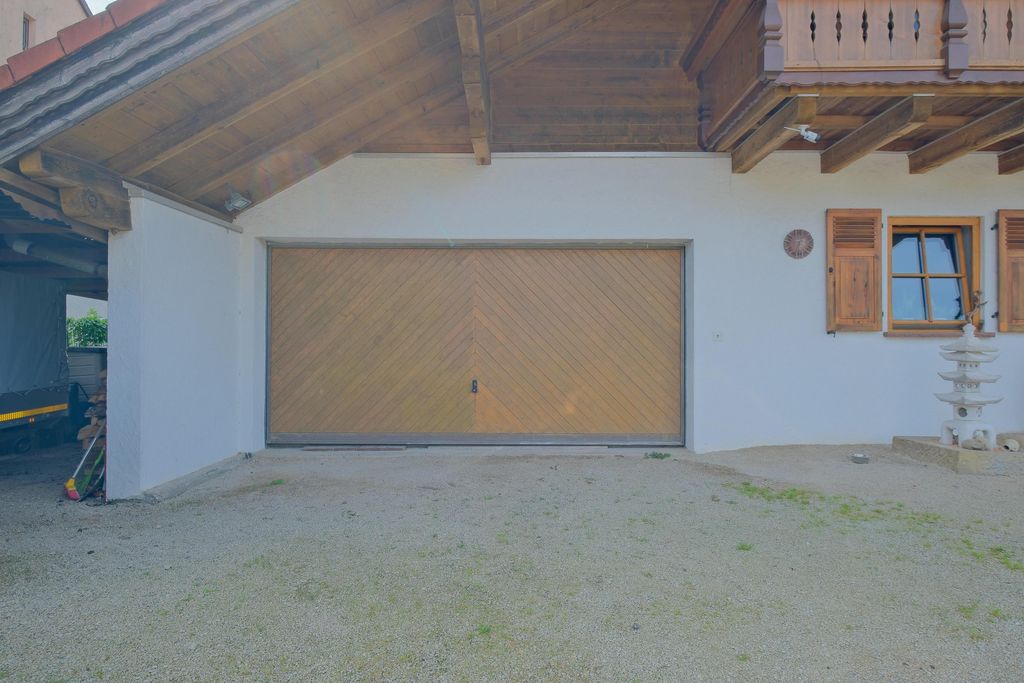 White garage with a large wooden double door and window with wooden shutters in a house featuring exposed wooden beams.