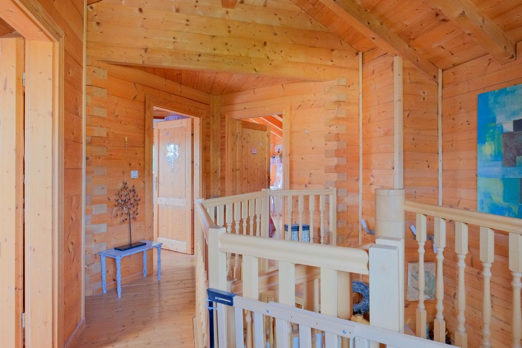 Interior of a house with natural wooden walls and floor, light wooden stair railing, and a small blue bench with a metal tree sculpture.