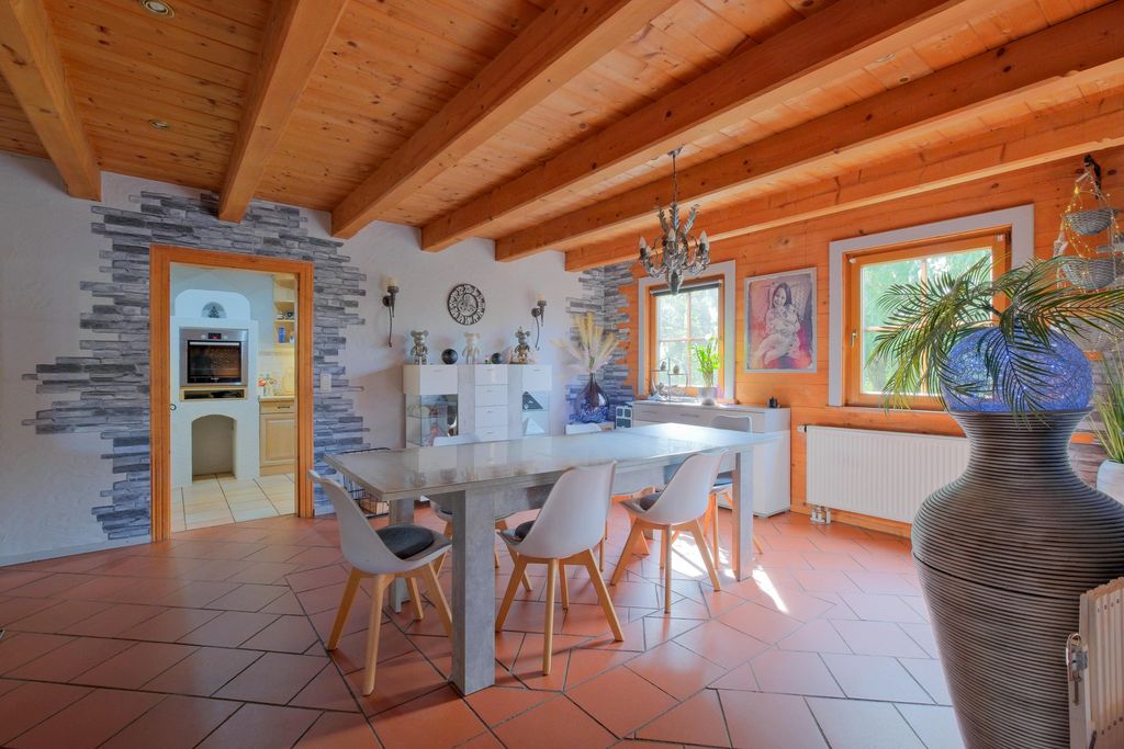 Modern dining area featuring wooden ceiling beams, a gray dining table, white chairs, and large windows letting in daylight.