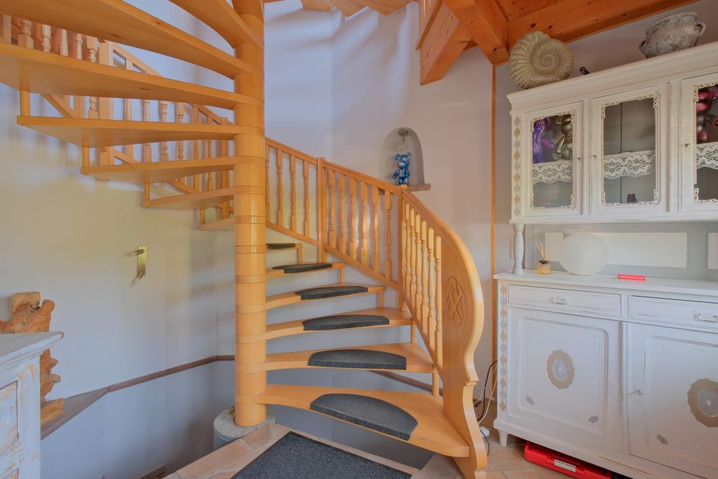 A wooden spiral staircase with carpet mats on the steps in a room with white walls and a white vintage cabinet.