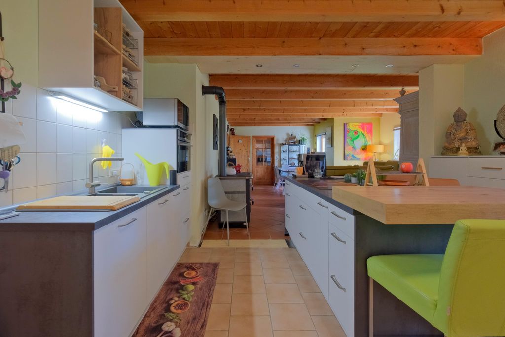 Modern kitchen with white cabinets, wooden ceiling, and a green chair at a countertop with a wooden top.