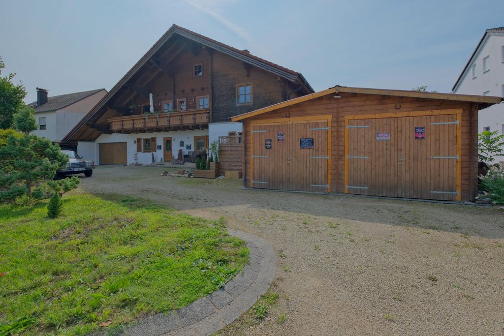 Large traditional house with balcony and double wooden door garage on a gravel driveway with lawn area in the foreground.