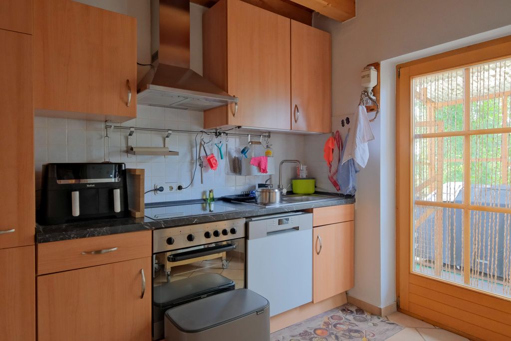 Modern kitchen featuring wooden cabinets, a stove with oven, a coffee machine, and a glass sliding door overlooking a terrace.