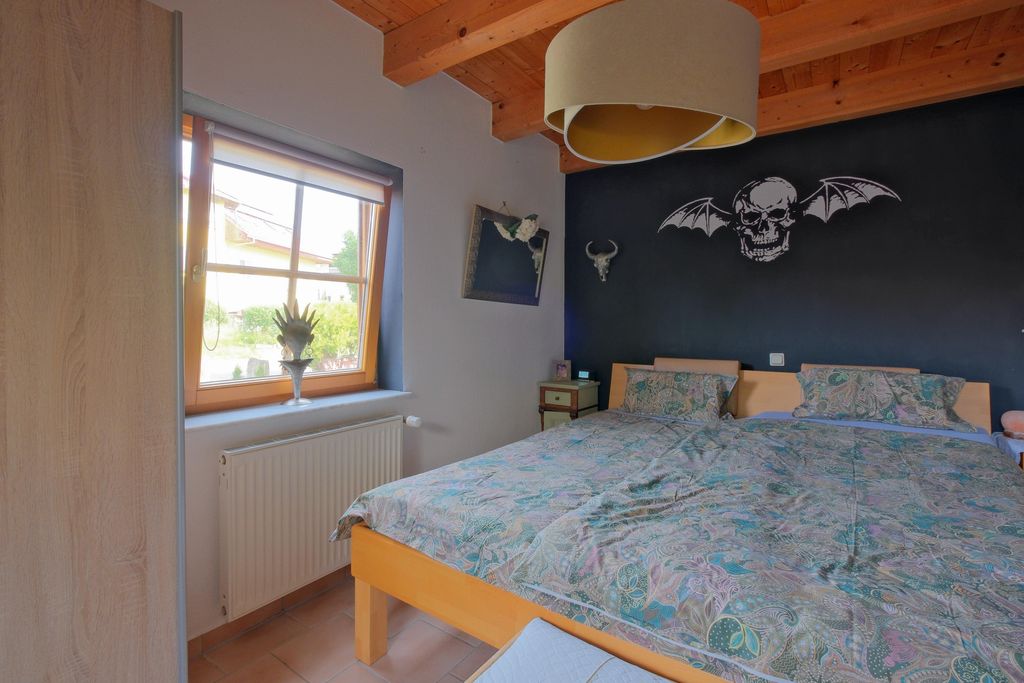 Bedroom with a double bed featuring floral patterned bedding, black wall decorated with a skull with bat wings, and a window overlooking the outside.