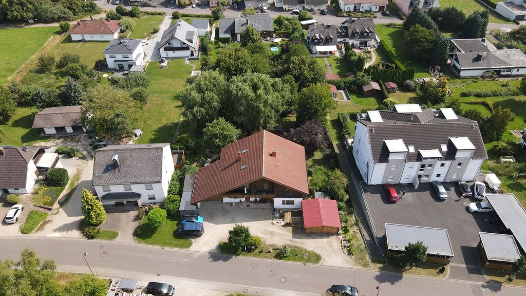 Aerial view of a residential area featuring single-family houses, gardens, and cars parked along a street on a sunny day.