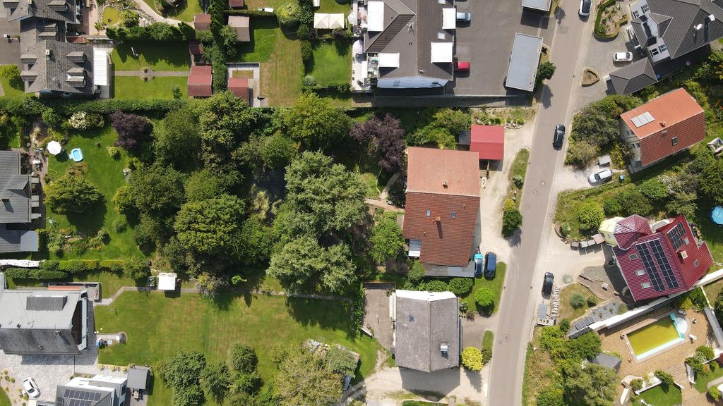 Aerial view of a quiet residential area with single-family houses, landscaped gardens, and a street with parked cars.