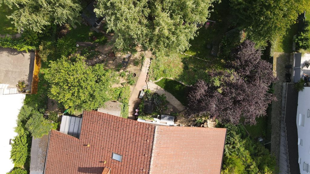 Bird's eye view of a garden with several trees and a house with a red tiled roof covering part of the image.