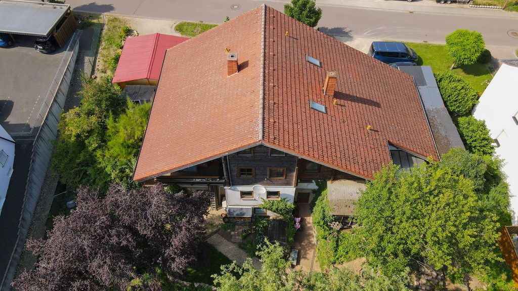 Aerial view of a residential house with a red tiled roof, surrounded by trees and a garden, located by a street with parked cars.