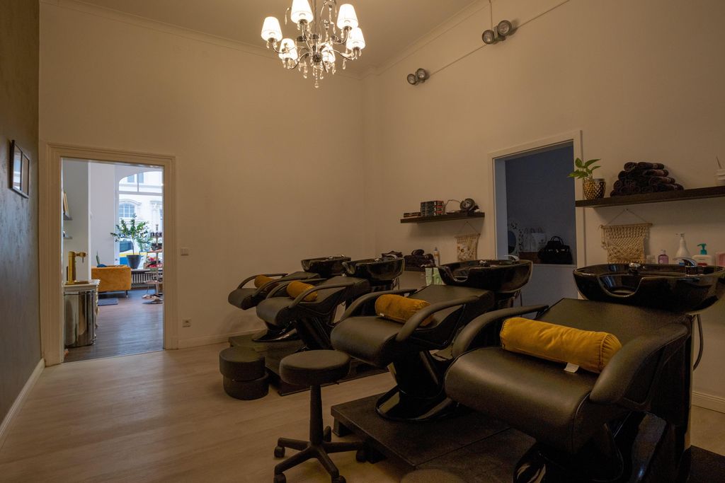 Interior of a hair salon with several black washing chairs equipped with yellow pillows and a chandelier hanging from the ceiling.