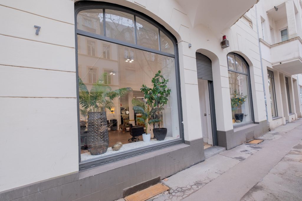 Street view with large arched windows of a building displaying indoor plants and interior furnishings.