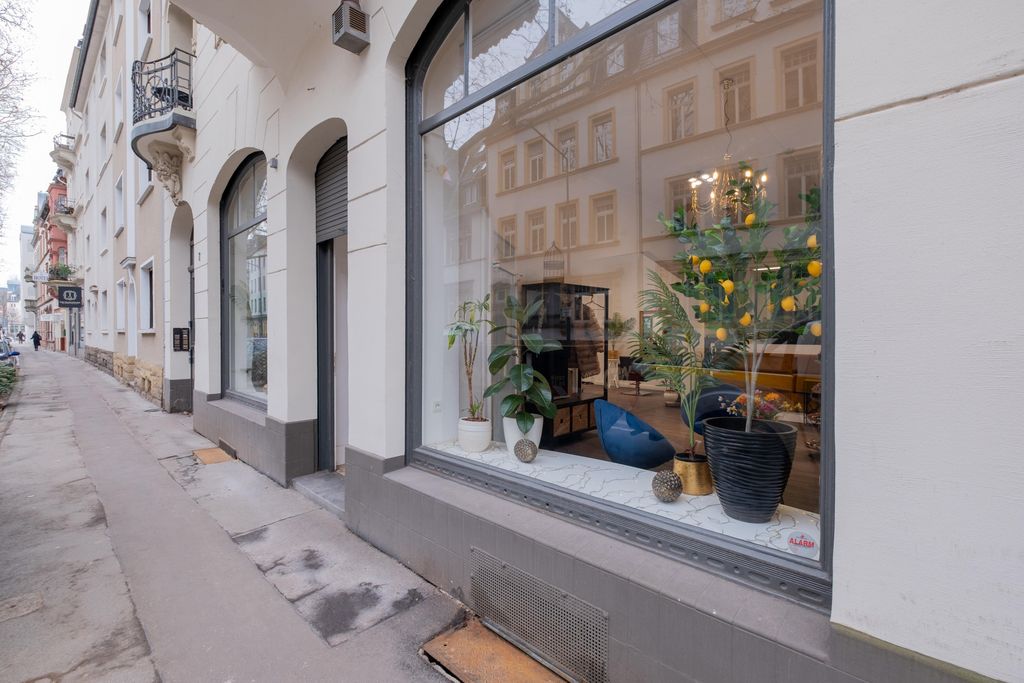 A street with old buildings and a shop window displaying various potted plants, including a tree with yellow fruits.