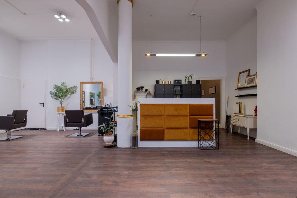 A modern hair salon with brown salon chairs, a reception desk with orange upholstery, and white walls.