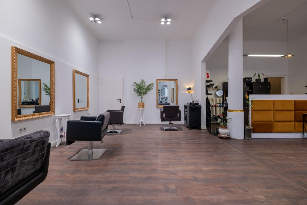 Modern hair salon with wooden flooring, large mirrors on white walls, and black salon chairs in a bright, spacious room.