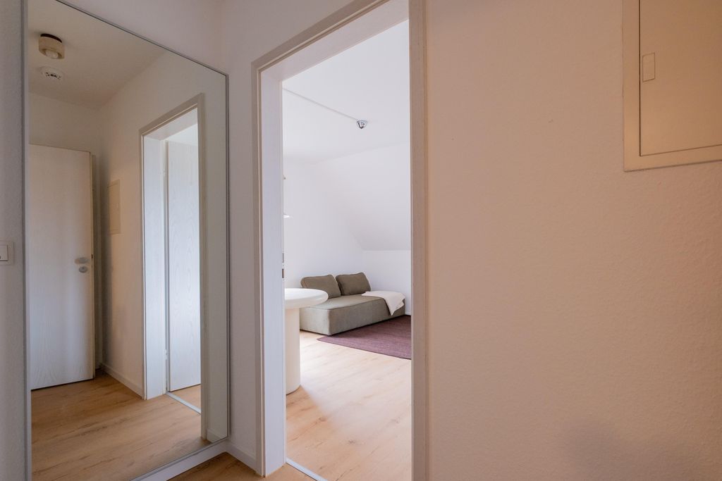 View through an open door into a living room with light wooden floors, a gray sofa, and a round white table.