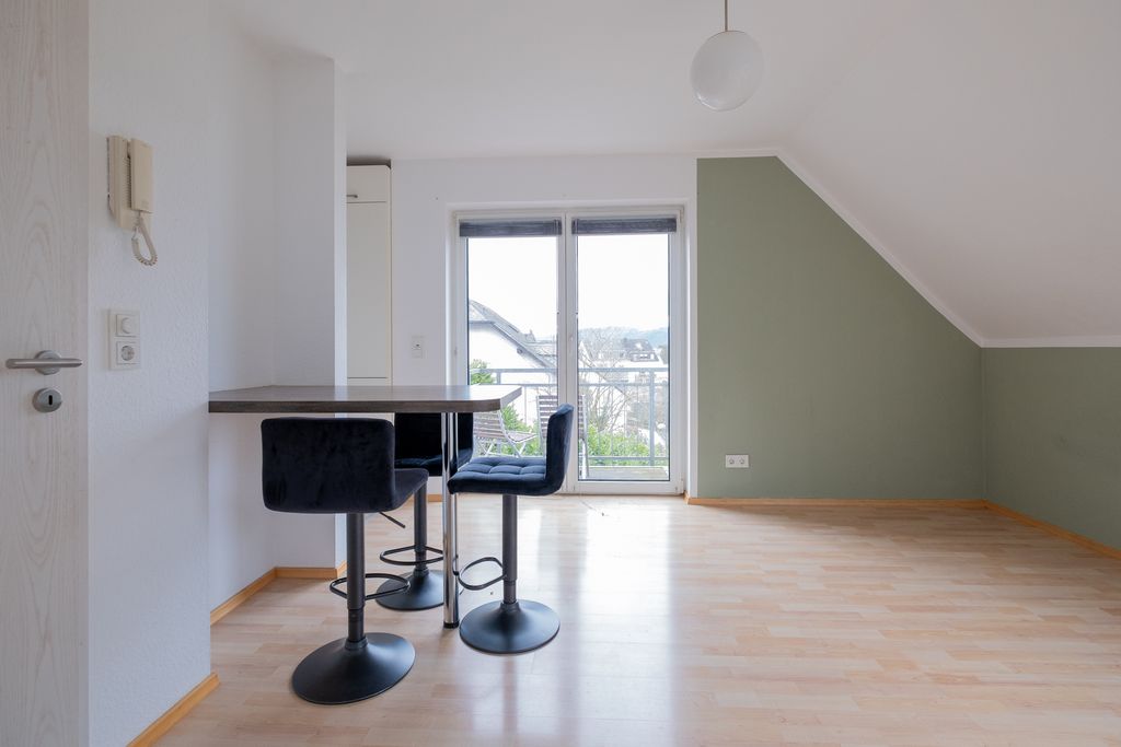 A bright, empty room featuring a small dining table with four modern bar stools in front of large glass doors overlooking the neighborhood.