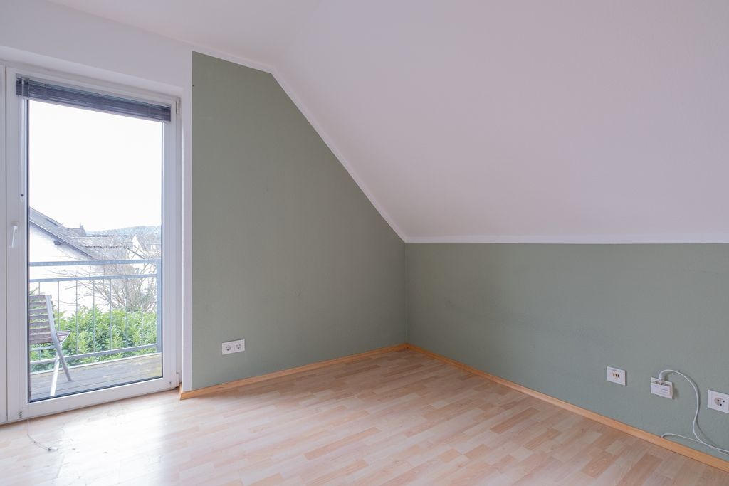 Empty room with wooden parquet floor, green wall, and large glass door overlooking a terrace and garden.
