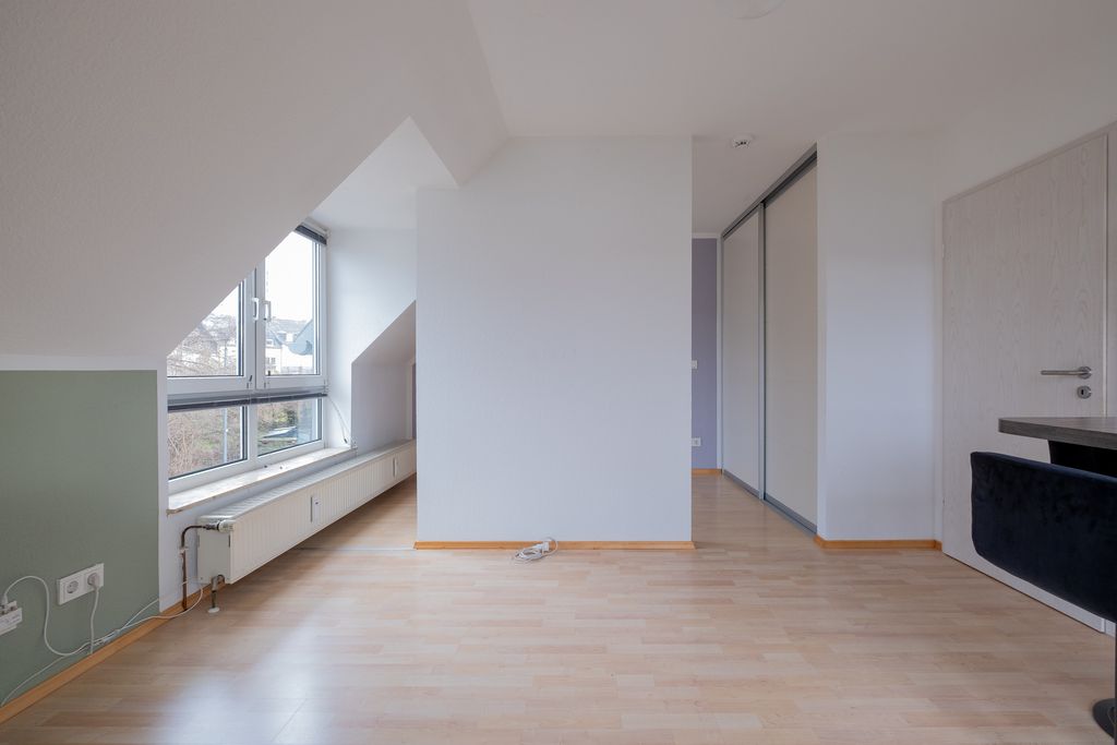 Empty room with light wooden floors, a green wall on the lower left, large windows, and a white wall in the center with a small object on the floor.