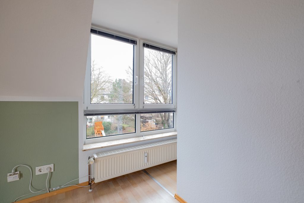 Room with slanted ceiling, a large window with white frames, a radiator beneath it, and a green wall section next to white walls.