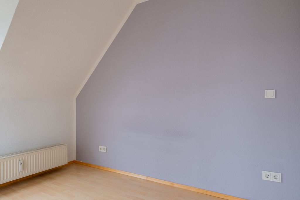 Empty room with light purple wall, white slanted ceiling, and wooden floor.