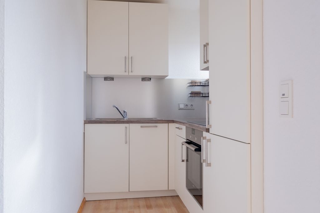 Small modern kitchen with white built-in cabinets, wooden countertops, and an oven installed in a narrow space.