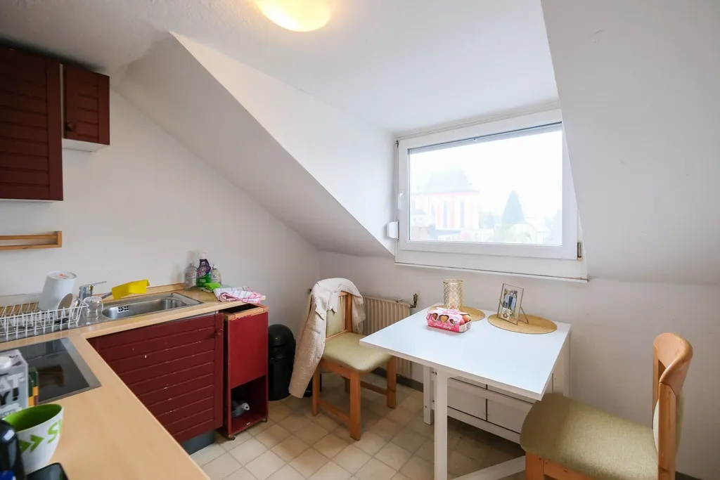Small kitchen with red cabinet, sink, two chairs, and a white table under a roof window.