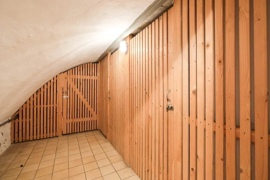 Hallway with sloped ceiling and closed wooden slatted doors, illuminated by a ceiling light.