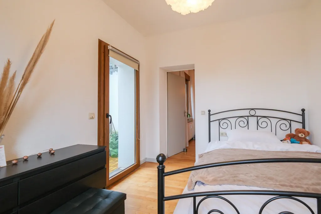 Bright bedroom featuring a black metal bed with a teddy bear on it, a dresser beside a glass door leading to an outdoor area.