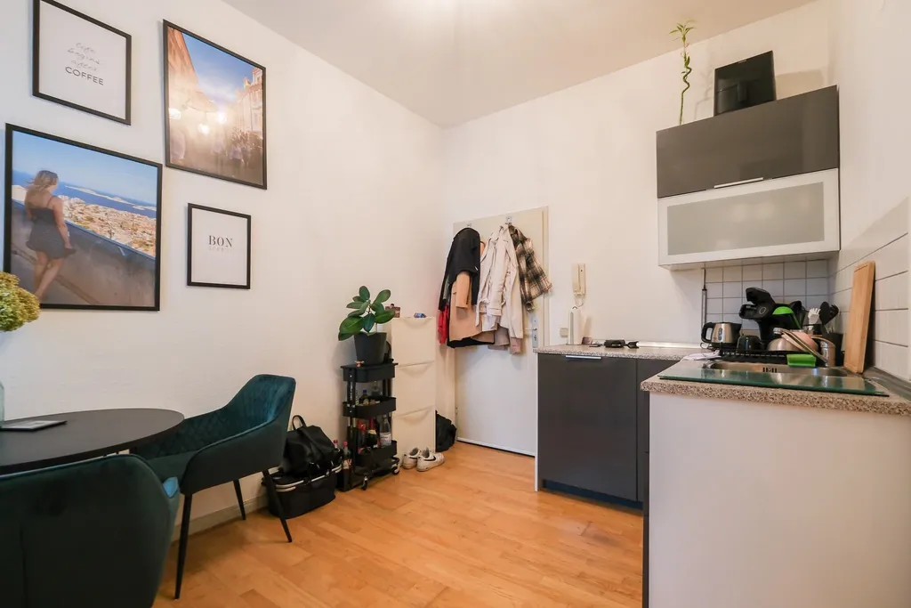 Modern apartment entrance area with coat rack, plants, beverage refrigerator, and framed pictures on the wall.