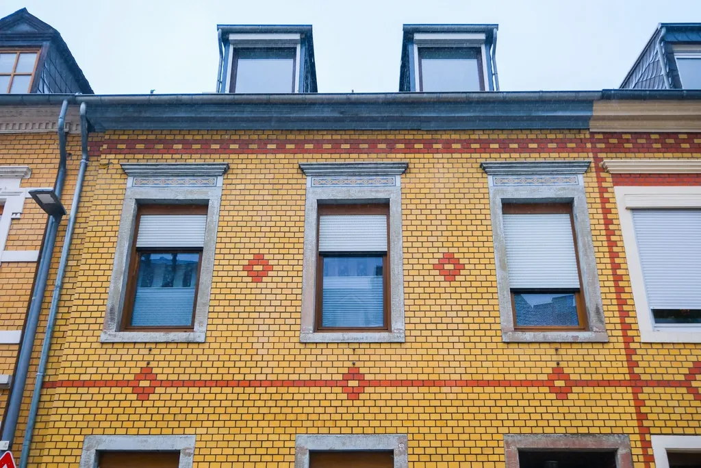 Facade of a yellow brick house with three windows and dormer windows under a blue sky.