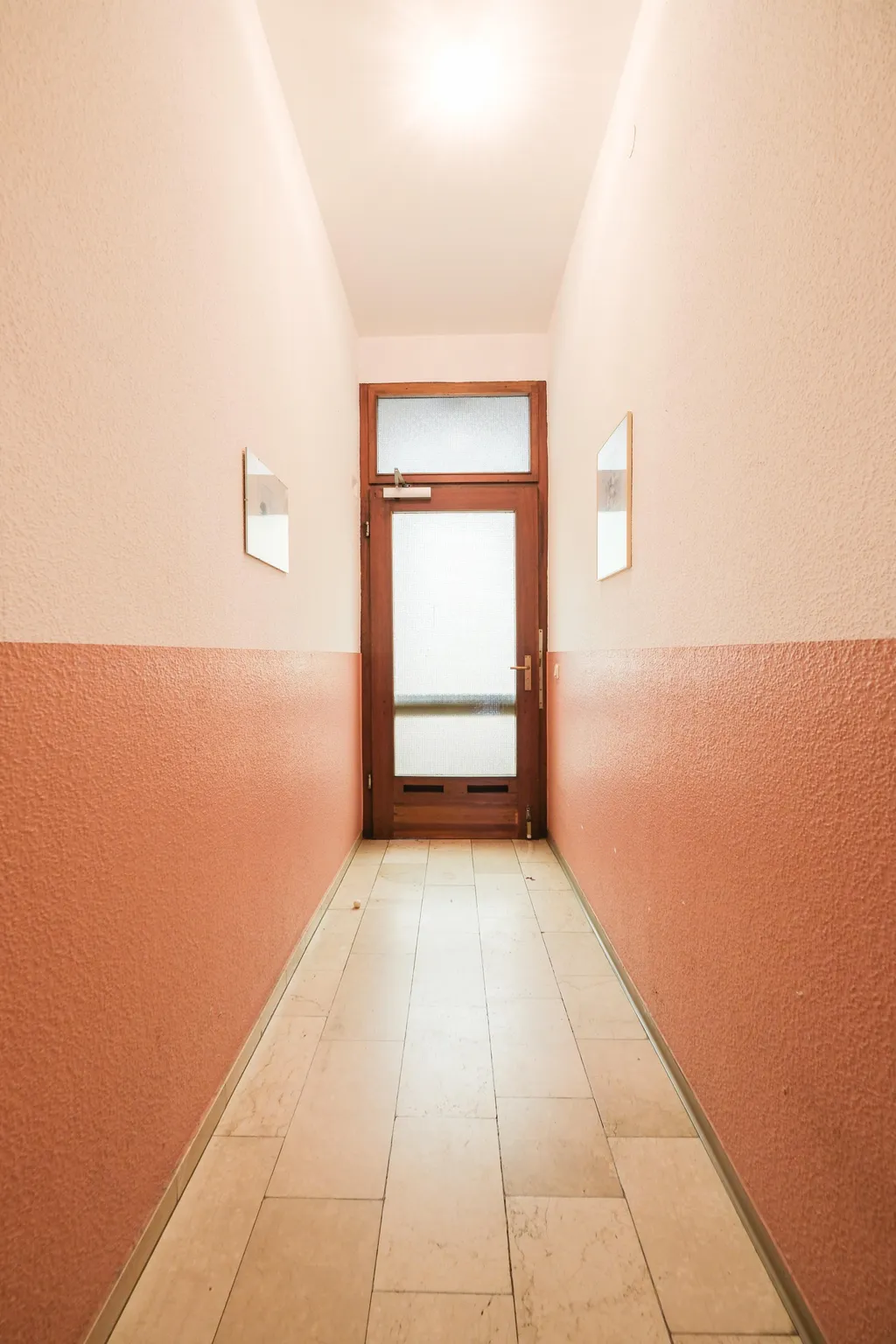Narrow hallway with half-height red walls and a door with a window at the end.