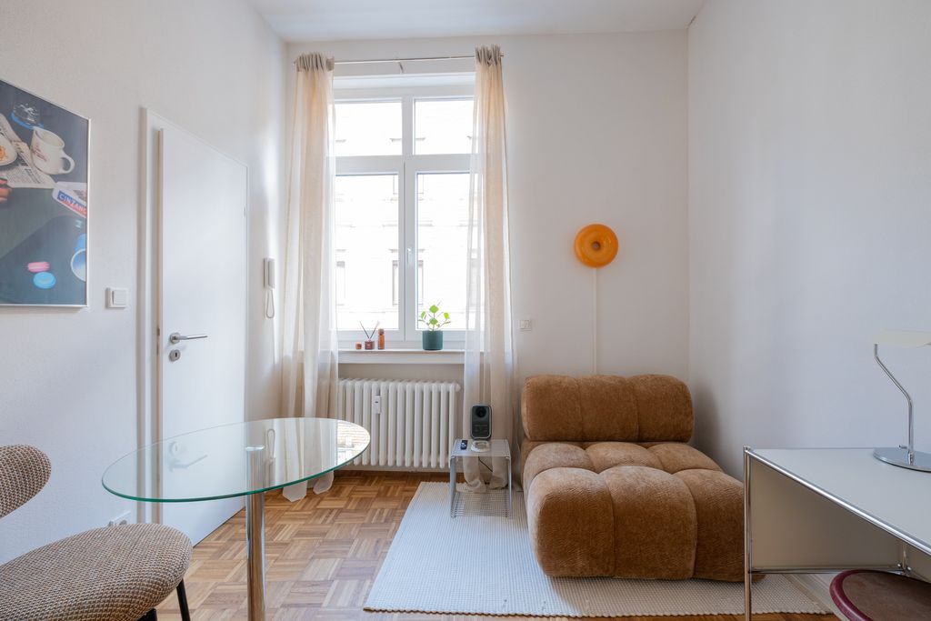 Bright living room with a large window, brown modern sofa, glass corner table, and white rug on parquet flooring.